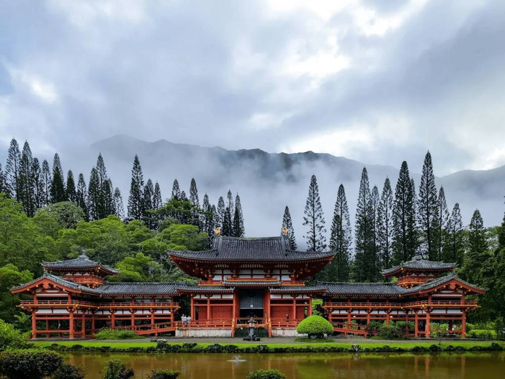 Traditional Japanese temple with red structure, surrounded by trees and misty mountains in the background.