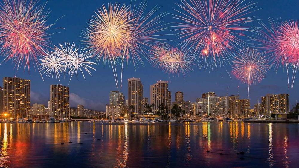 Fireworks over a city skyline reflected in water at night.