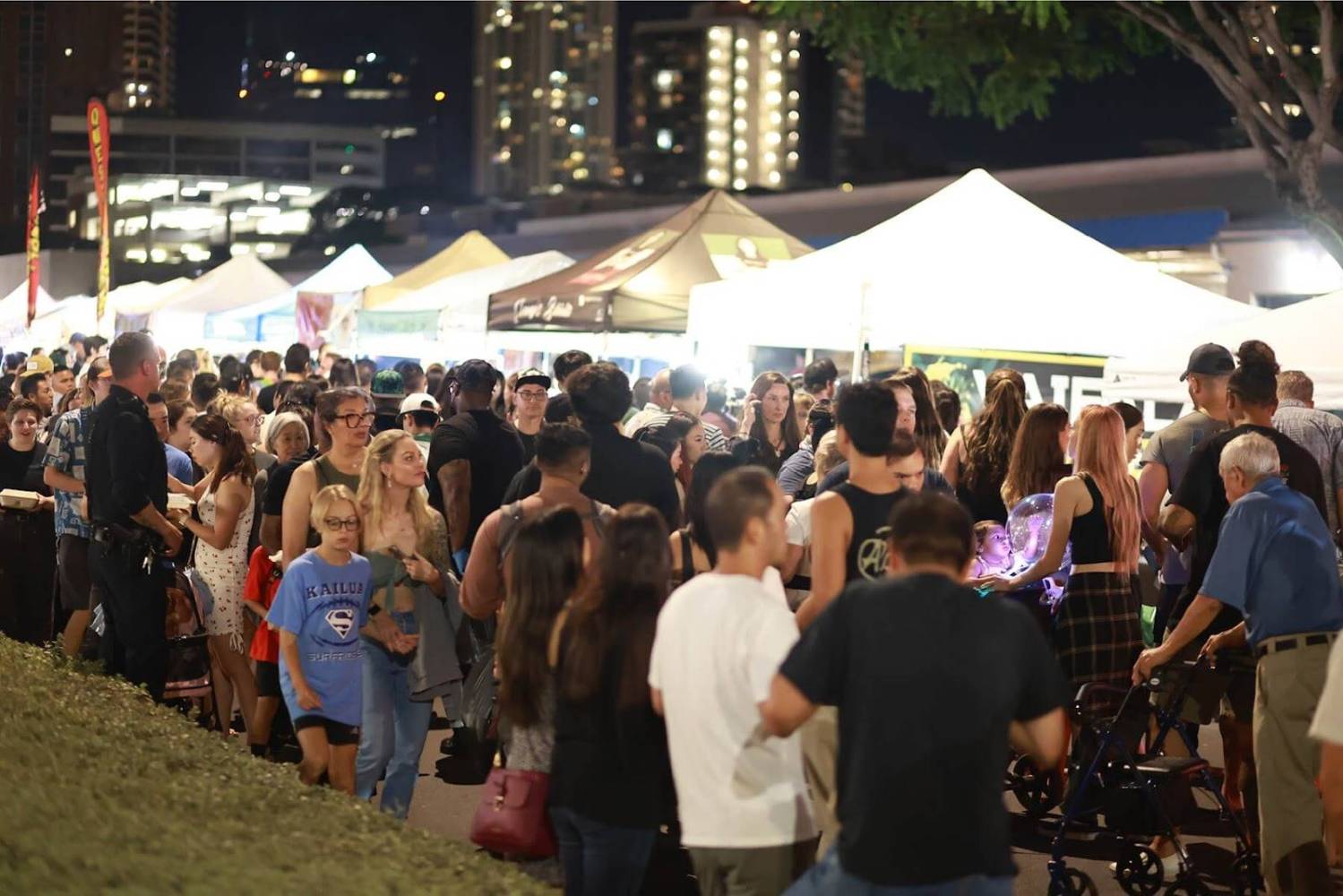 Crowded night market with tents and people walking, chatting, and browsing stalls.