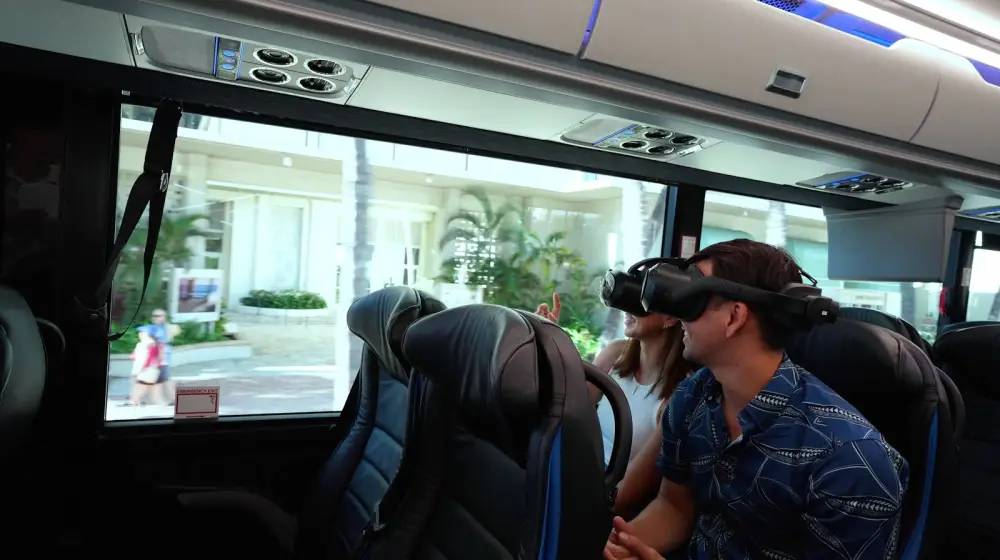 Two people on a bus wearing VR headsets near a window.