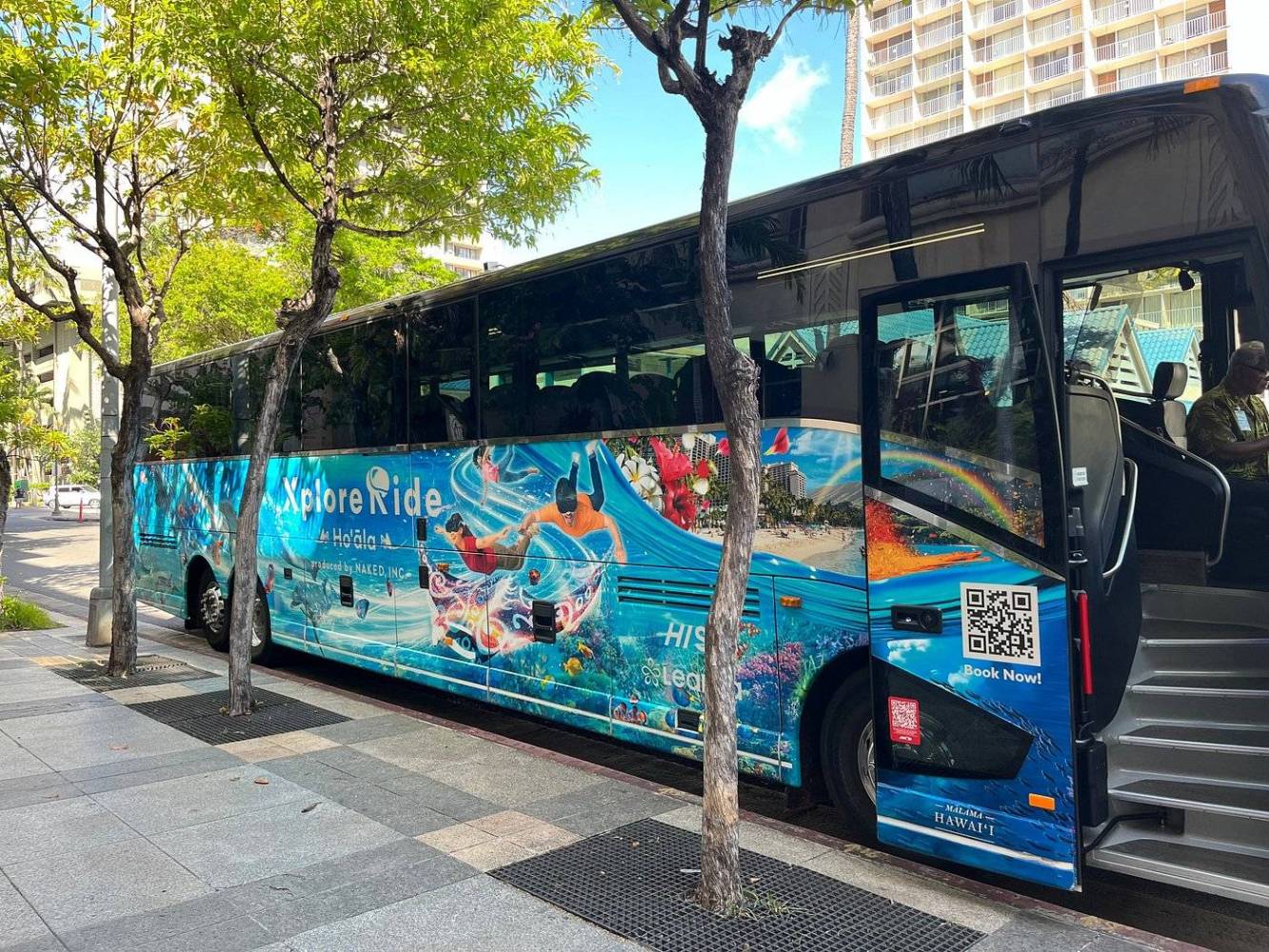 Colorful bus with beach graphics parked on city street near trees.