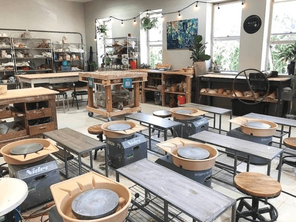 Pottery studio with wheels, worktables, and shelves of materials.