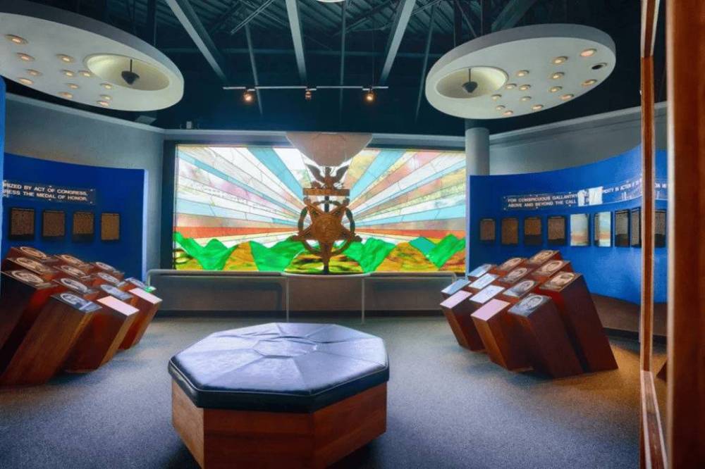 Museum exhibit with wooden displays, plaques, and a large stained-glass window depicting colorful patterns.