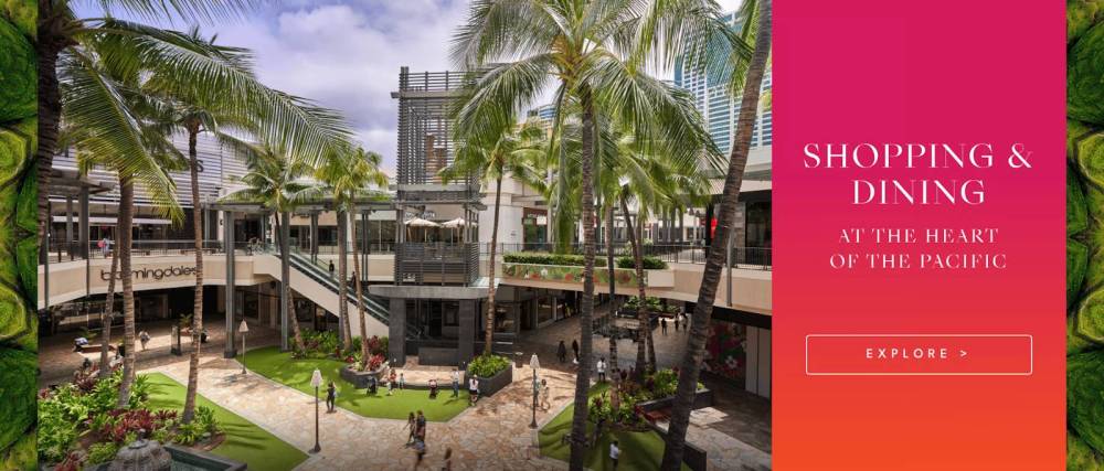 Outdoor mall scene with palm trees, shops, and dining area under cloudy sky.