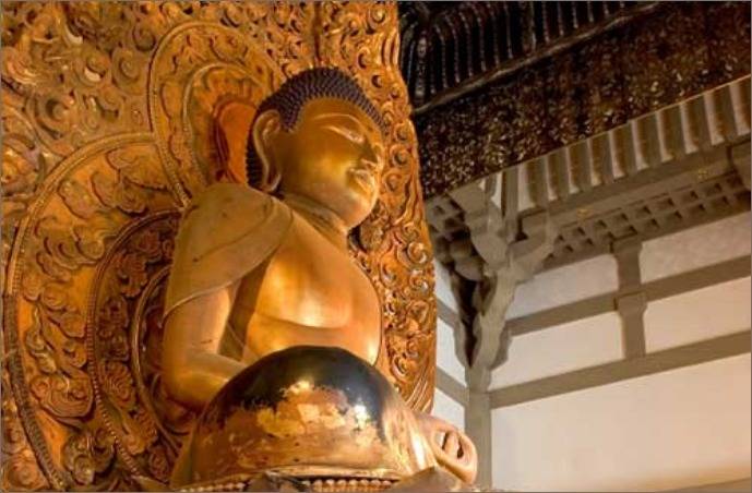 Golden Buddha statue inside an ornate temple setting with detailed carvings.