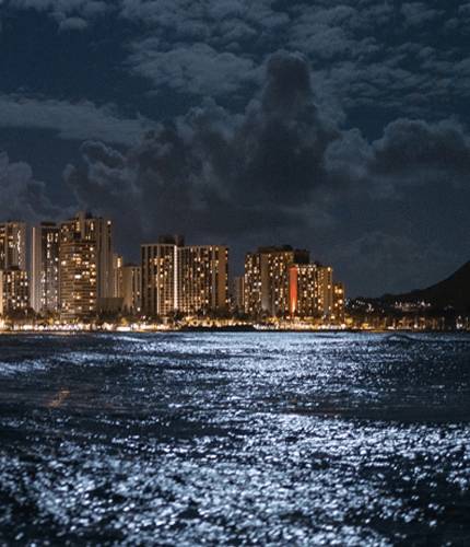 City skyline at night with illuminated buildings and reflections on the water.