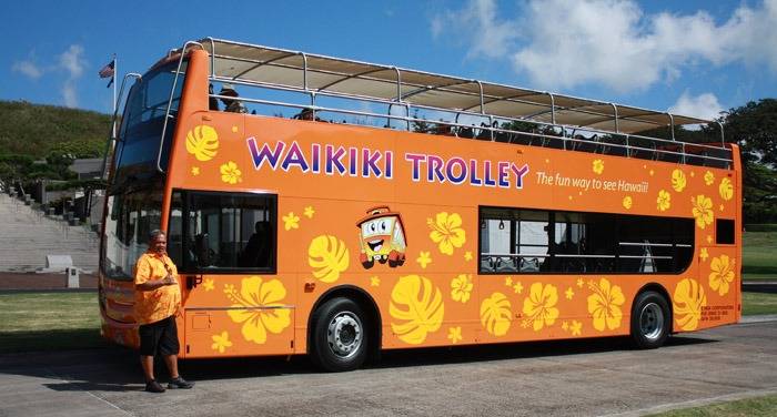 Orange double-decker bus with 'Waikiki Trolley' and floral designs parked outdoors.
