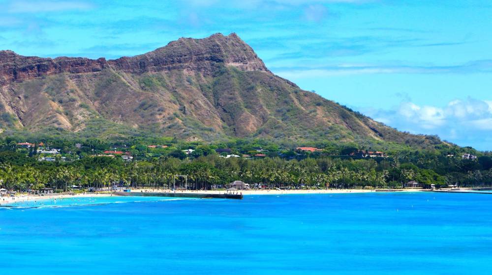 Scenic view of Diamond Head mountain with beach and blue ocean in foreground.