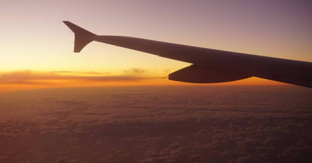 Airplane wing silhouetted against a vibrant sunset sky with clouds below.