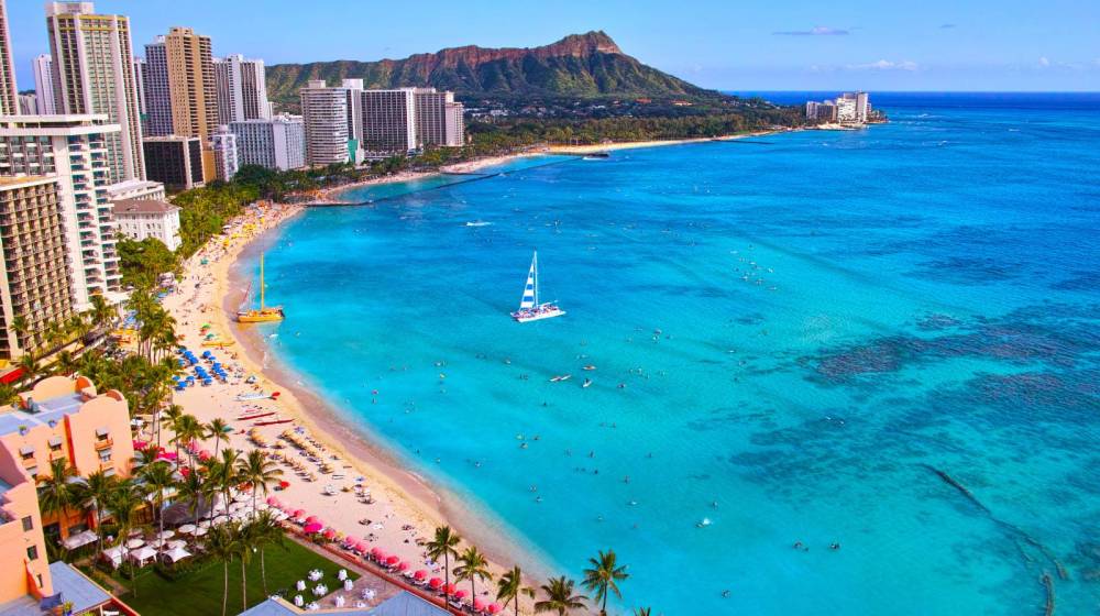 Aerial view of a beach with skyscrapers, clear blue water, and a mountain in the background.