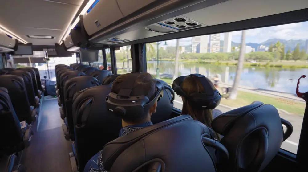 Bus interior with passengers wearing VR headsets, scenic view outside.