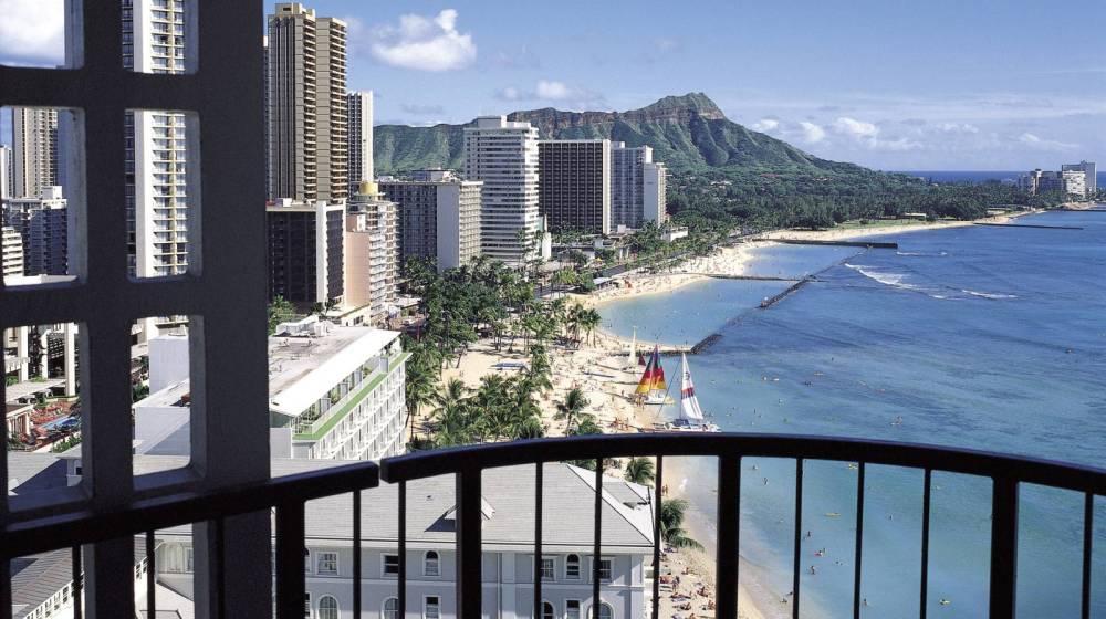 Cityscape with beach, ocean, and mountains seen from a high balcony on a clear day.
