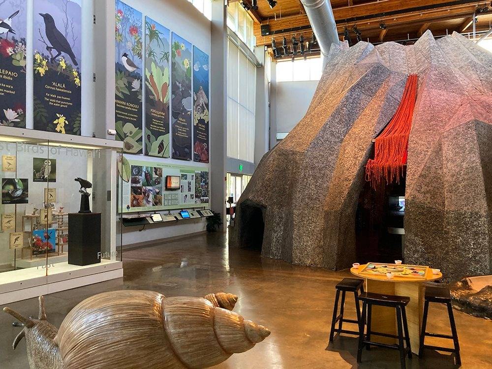 Museum exhibit with large volcano model, educational panels, and seating area.