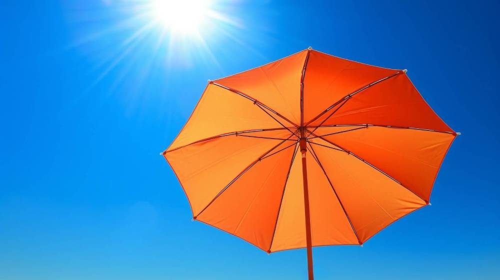 Orange umbrella against a clear blue sky with bright sun.