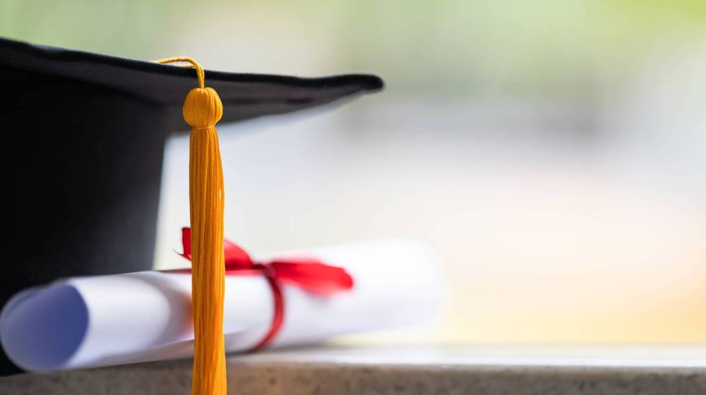 Graduation cap and diploma with red ribbon on a table.
