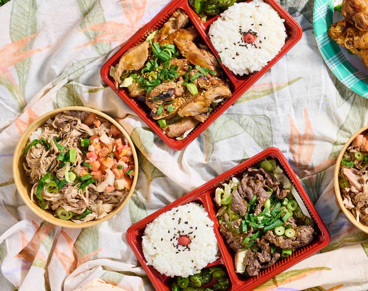 Assorted bento boxes and bowls with rice and meat on a floral tablecloth.