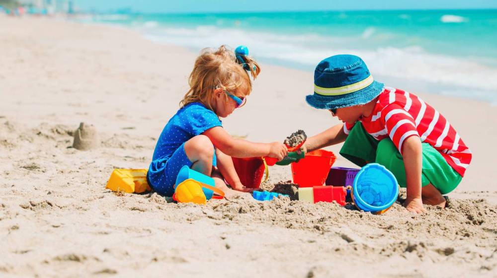 Two children playing with sand toys on a sunny beach near the ocean.