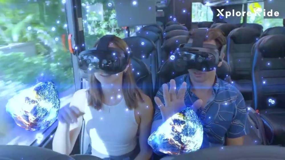 Two people on a bus wearing VR headsets interacting with virtual globes.