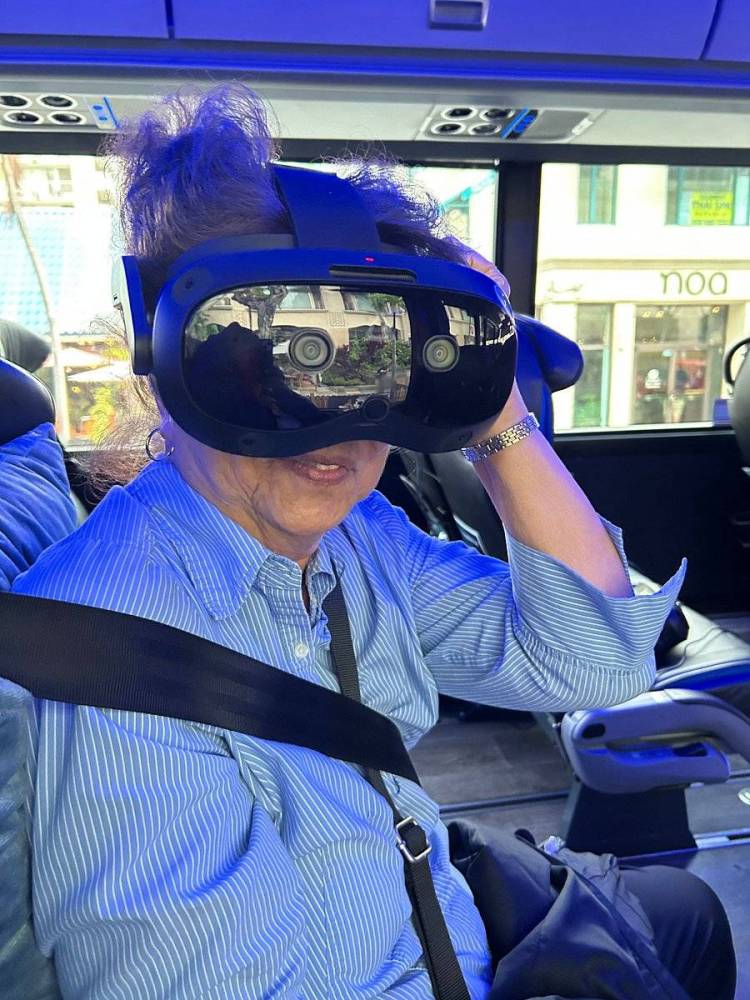 Person wearing a VR headset, seated on a bus with seatbelt fastened.