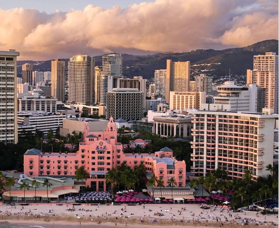 Pink hotel and city skyline at sunset with mountains.