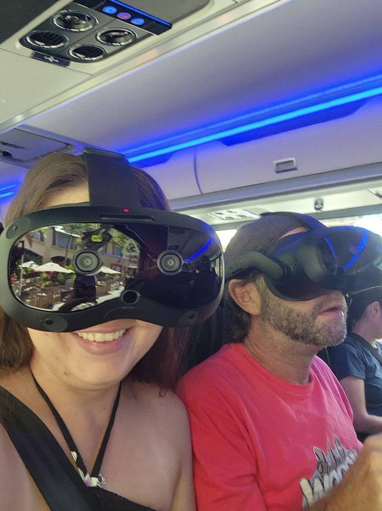 Two people wearing VR headsets in a vehicle, one smiling.