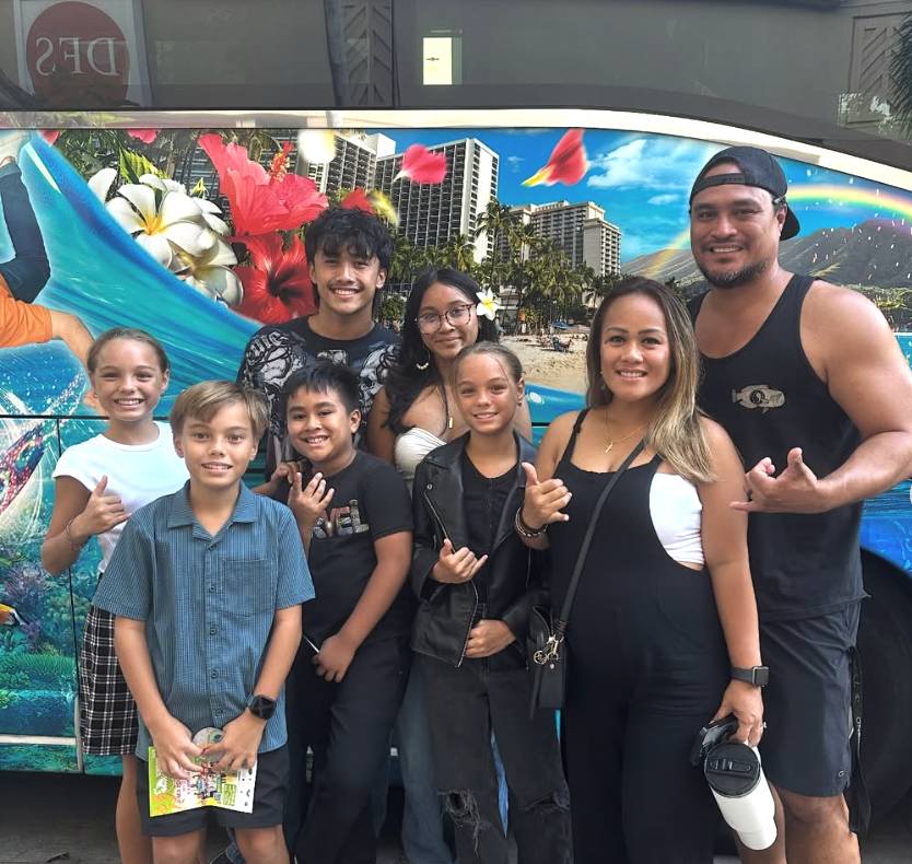 Group of people smiling in front of a vibrant, floral-themed bus.