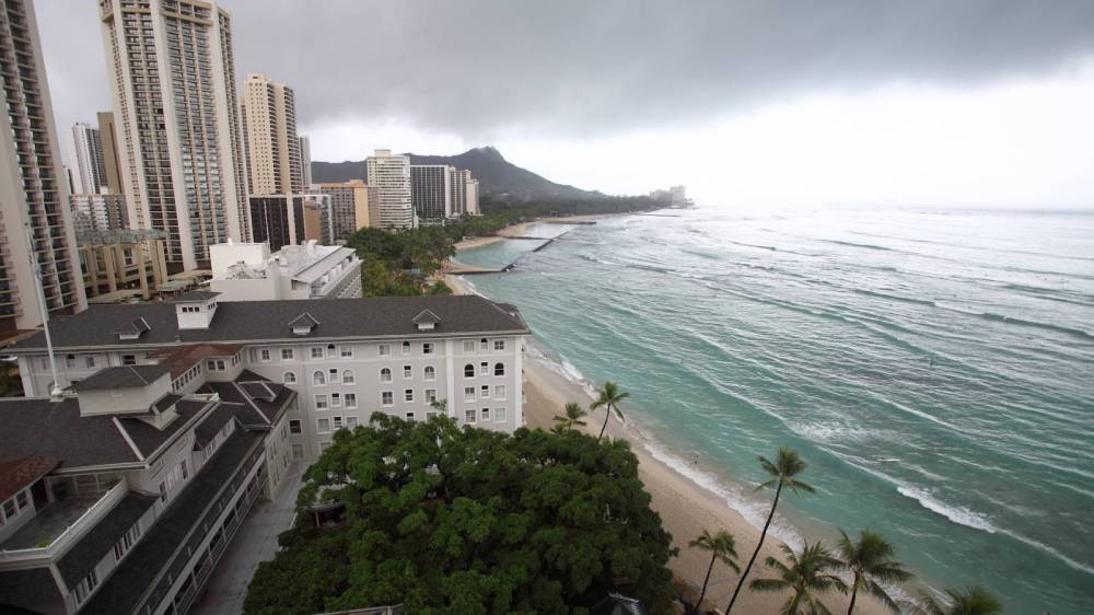 Tall buildings by a beach with calm ocean waves and overcast sky.