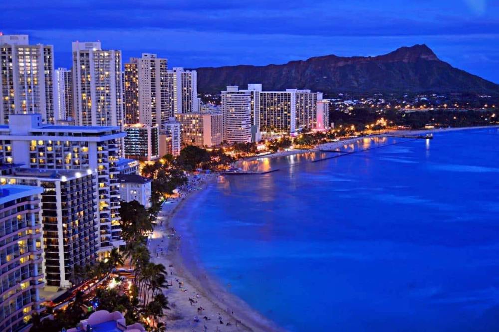 City skyline at dusk with tall buildings beside a beach and ocean.
