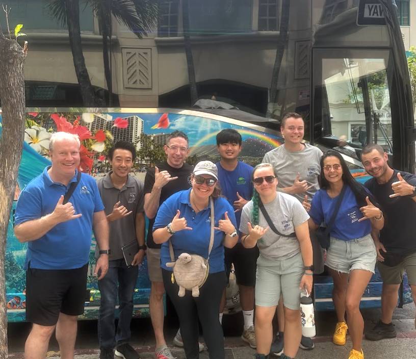 Group of people smiling and posing in front of a colorful bus.