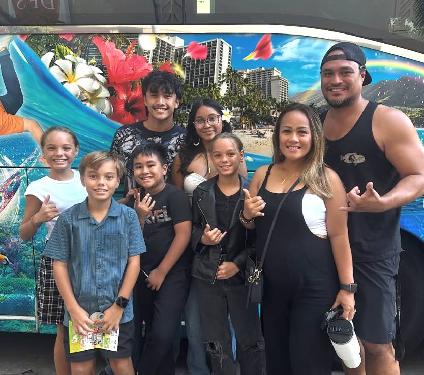 Group of people smiling and making shaka signs in front of a colorful van.