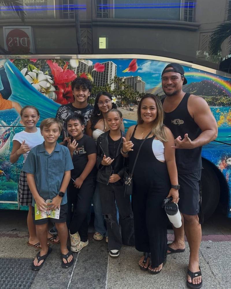Group of eight people smiling in front of a colorful bus with tropical design.