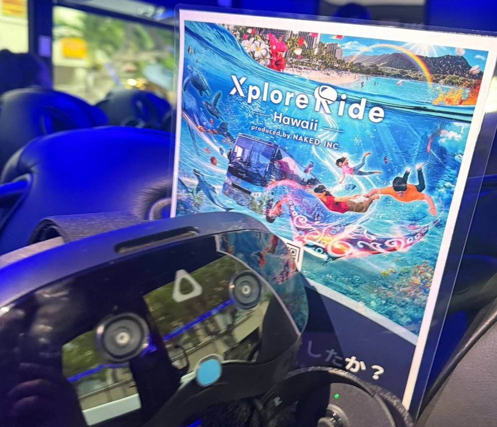 Virtual reality headset next to colorful Xplore Ride Hawaii poster on bus seat.