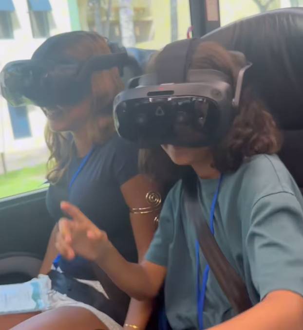Two people wearing VR headsets and sitting on a bus.