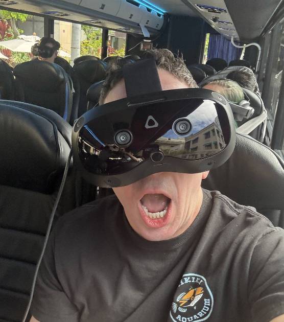 Man wearing a VR headset, sitting on a bus with mouth open.