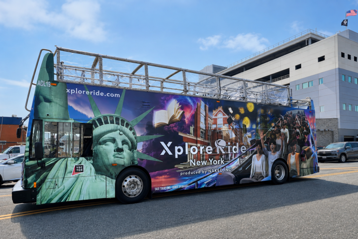 Colorful open-top tour bus with NYC landmarks images, parked by office buildings.