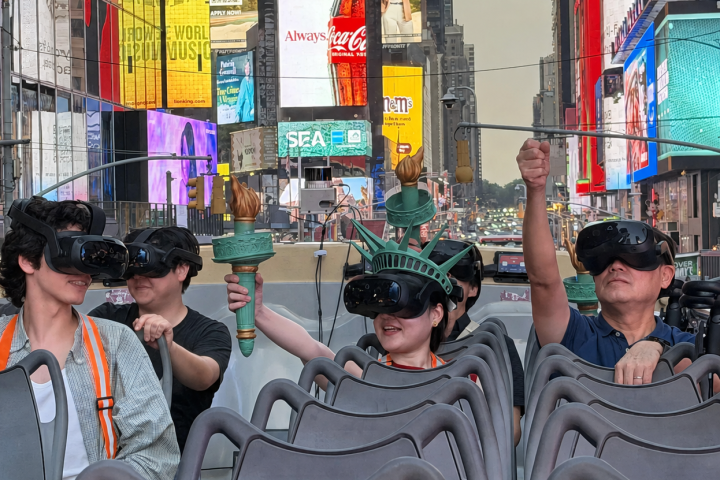 People in VR headsets on a city tour bus, holding small replicas of the Statue of Liberty's torch.