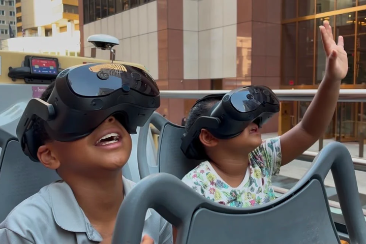 Two children enjoy VR headsets, smiling and reaching out.