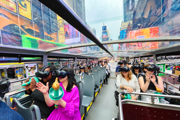 People wearing VR headsets on a glass-roofed tour bus in a city.