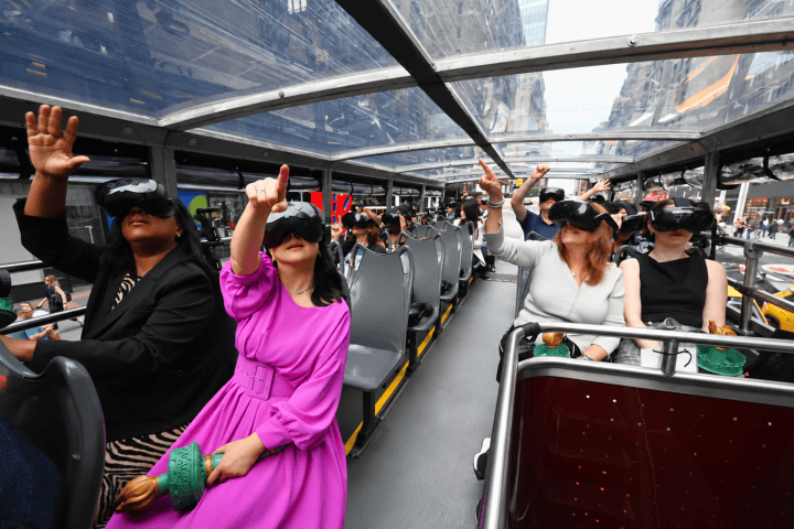 People wearing VR headsets on a double-decker bus with a glass roof.