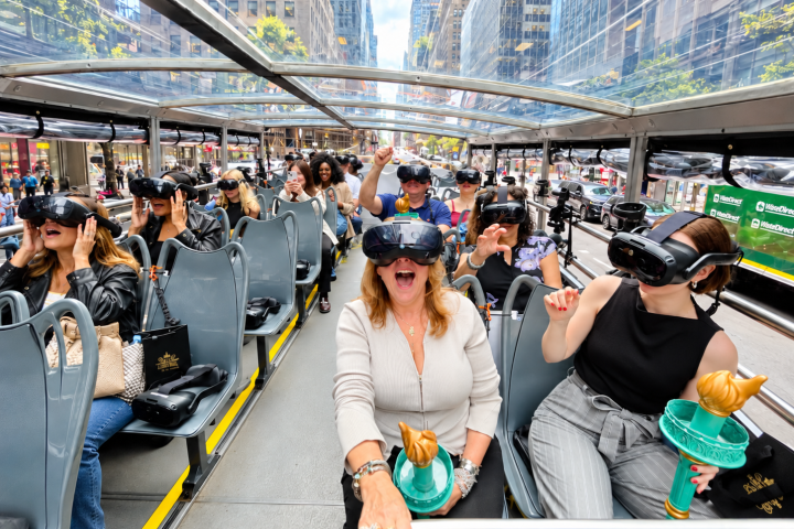 People on a bus wearing VR headsets, holding mini Statues of Liberty.