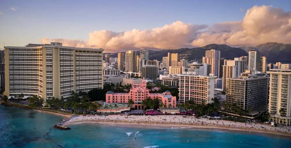 Beachfront cityscape with tall buildings and pink hotel at sunset.